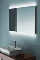 Ein rechteckiger Spiegel mit integrierter LED-Beleuchtung, montiert über einem weißen Waschbecken. Der Bereich ist in sanften Farben gehalten und vermittelt eine moderne Badatmosphäre. Ideal Standard.